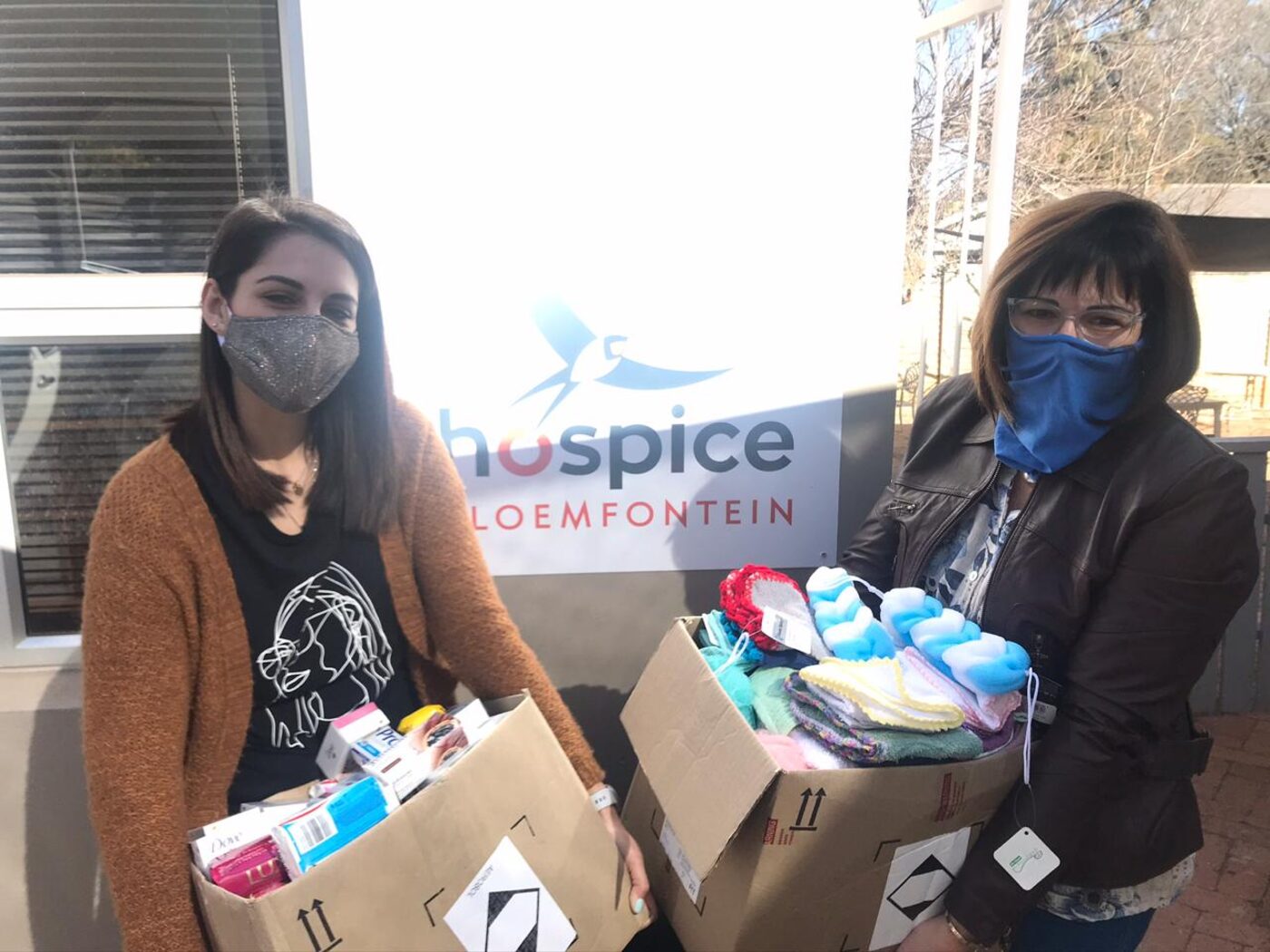 Twee ondersteuners met bokse vol skenkings voor 'n Hospice Bloemfontein-banier